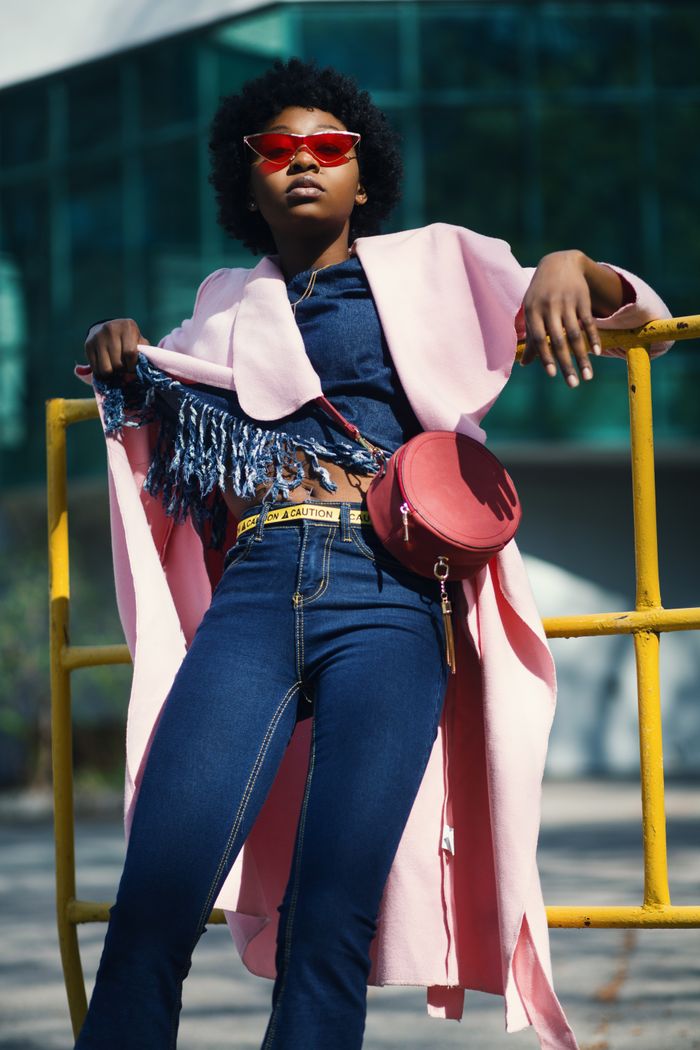 Fashionable portrait of a young woman in denim and pink coat, outdoors in sunlight.