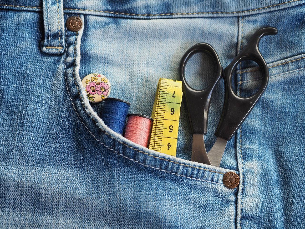 why-choose-us-img Close-up of sewing accessories in a denim pocket, featuring threads, scissors, and measuring tape.