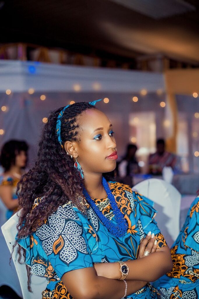 Stylish woman in vibrant traditional African attire sitting at an indoor event, looking thoughtful.