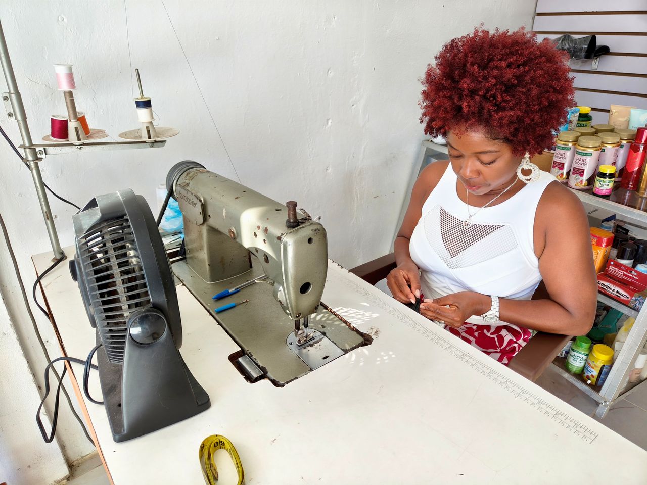 A woman tailor focuses on sewing fabric in a well-equipped sewing shop.