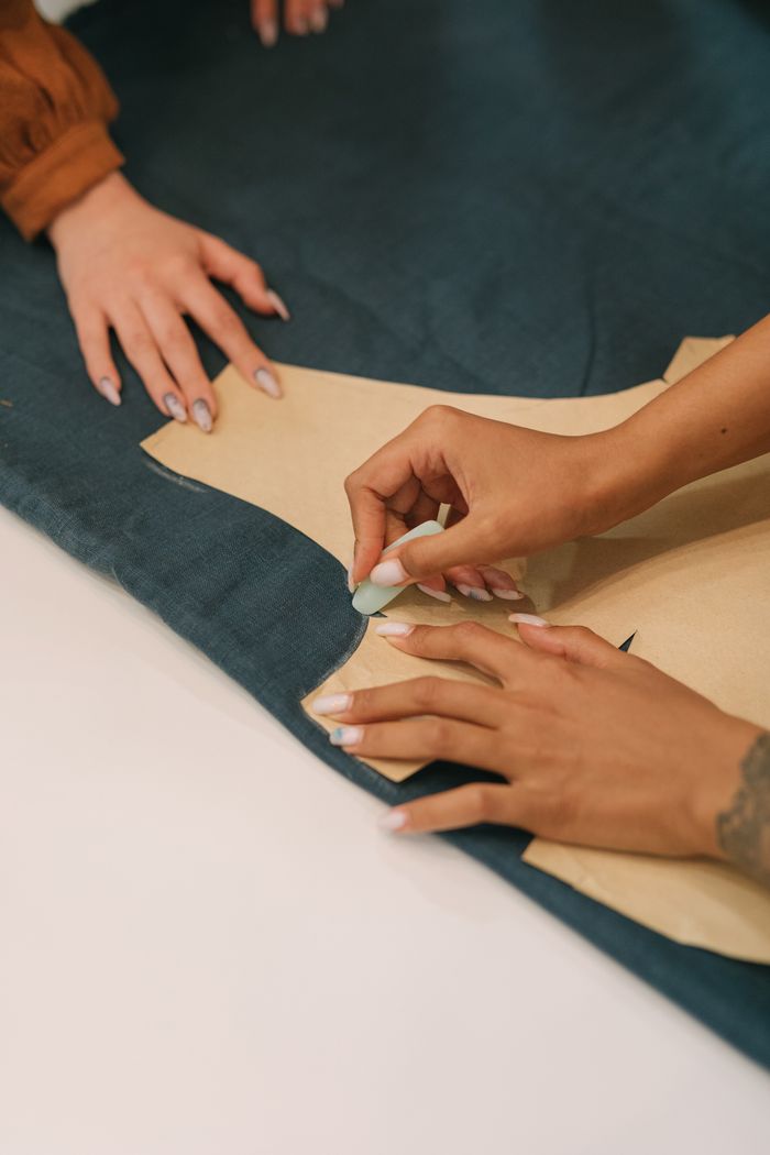 cta-image Close-up of hands marking a garment pattern, showcasing the craft of tailoring.